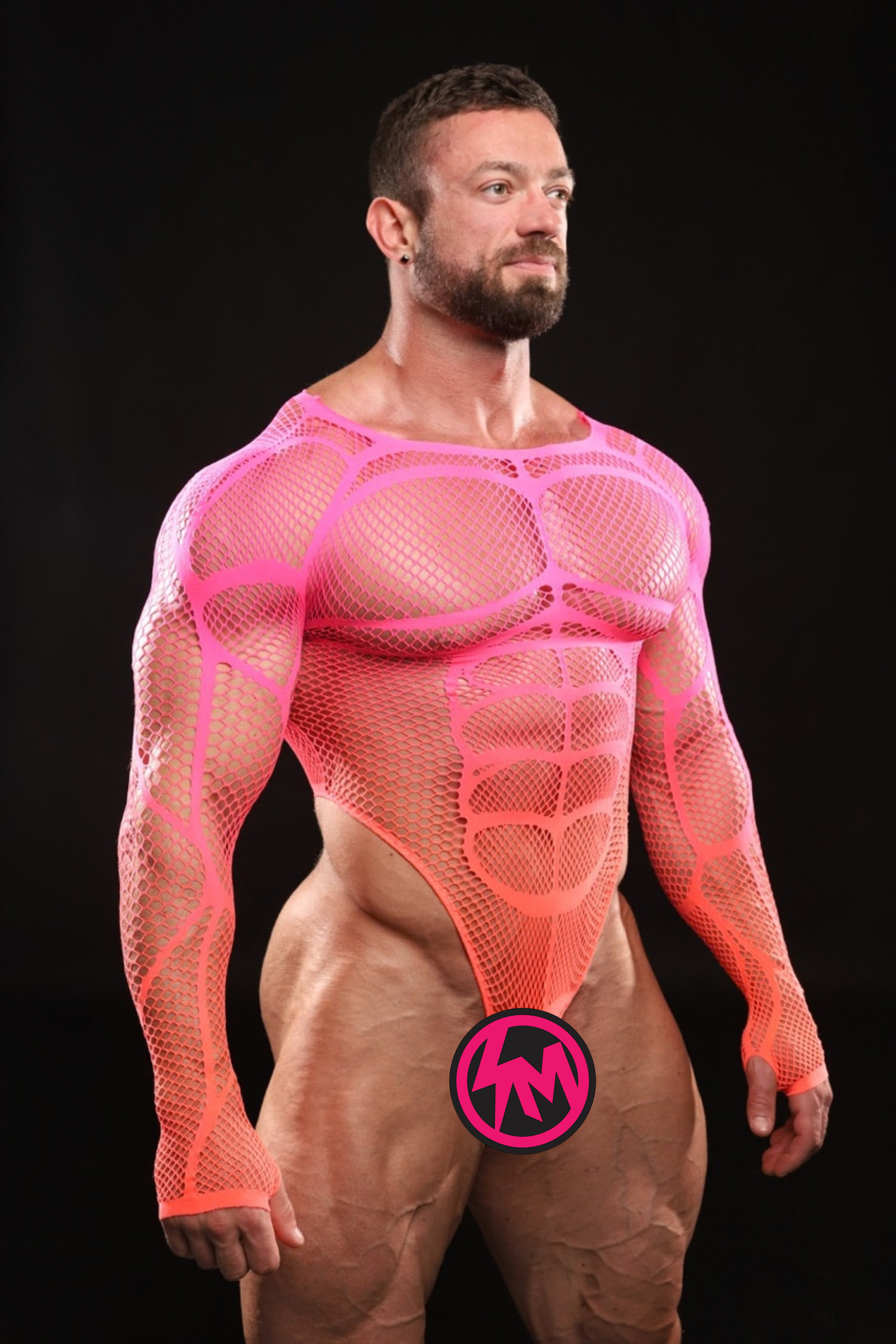 A muscular man wearing a bright neon pink mesh bodysuit with a high neck and long sleeves, posed against a solid black studio background. A circular pink and black logo is overlaid near the bottom center.