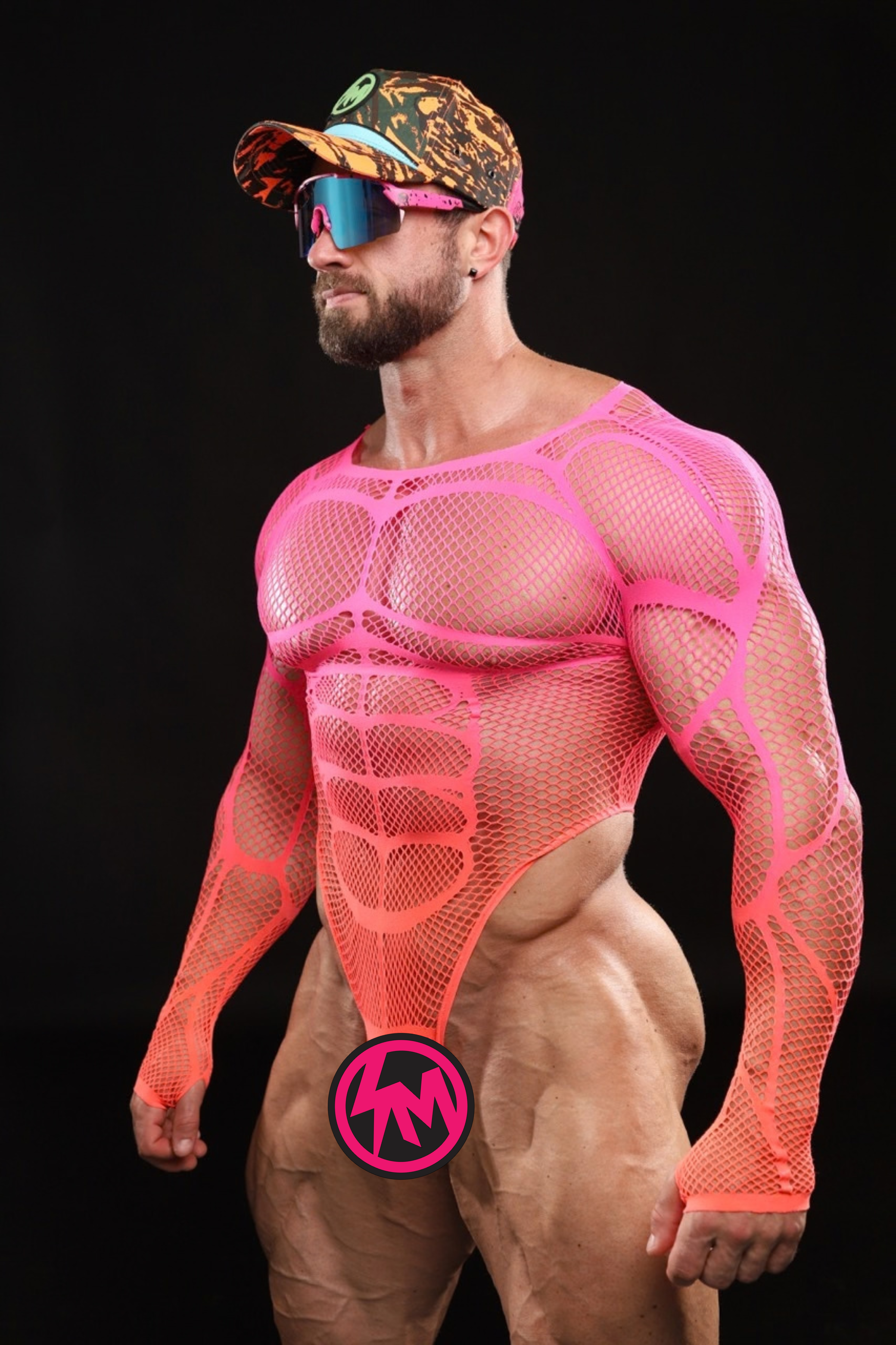A muscular man wearing a neon pink mesh body suit with long sleeves, an orange camo cap, and pink, tinted sunglasses, posed against a solid black background.
