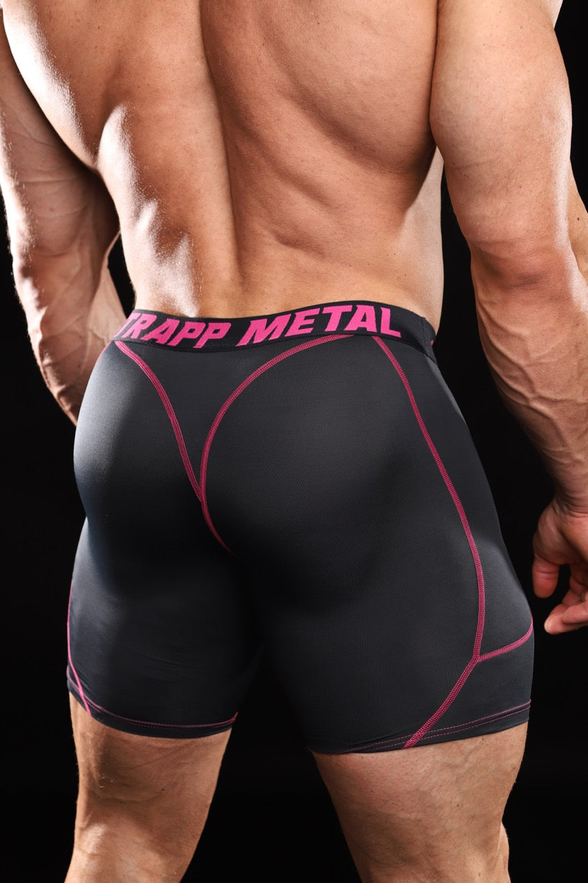 Rear view of a muscular man wearing black compression shorts with pink stitching and a pink and black waistband that reads 'STRAPP METAL'.
